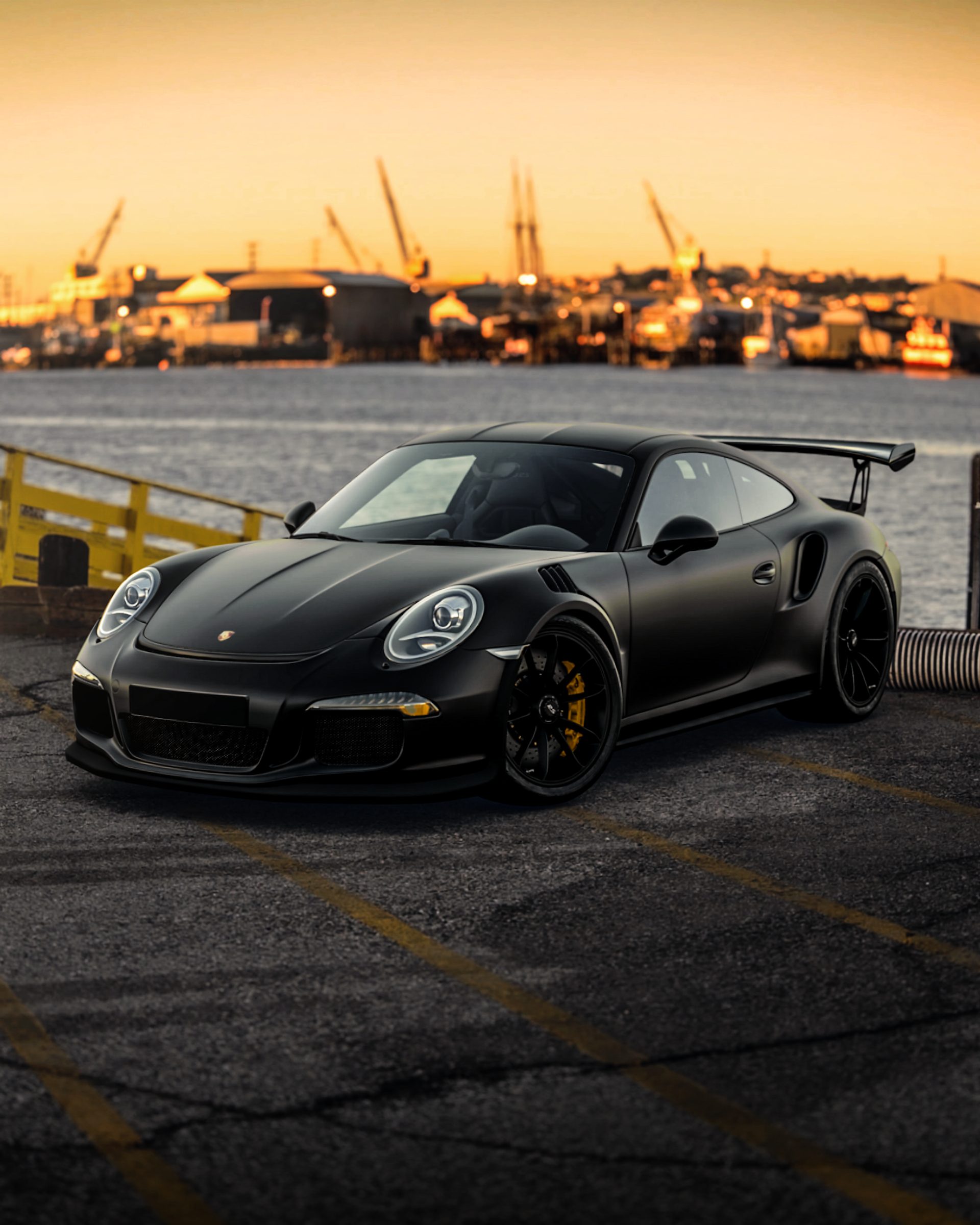 Porsche 911 GT3 noire, vue de trois quarts avant, au crépuscule sur un quai portuaire